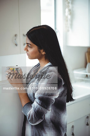 Thoughtful woman holding cup tea in kitchen at home