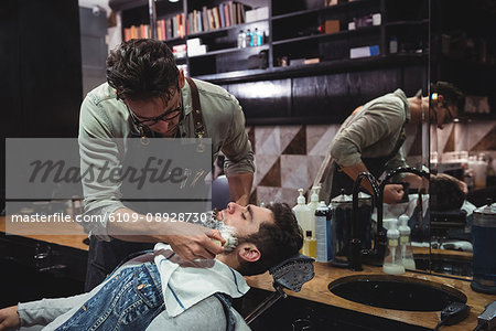 Barber applying cream on clients beard in baber shop