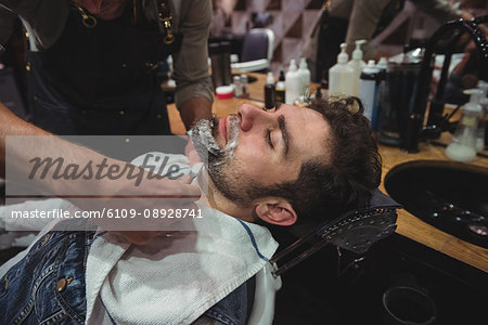 Man getting his beard shaved with razor in barber shop