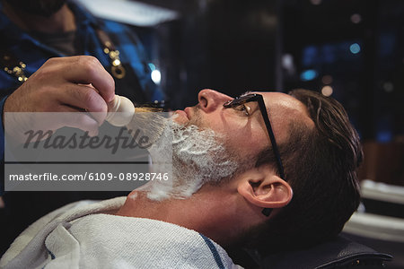 Mid section of barber applying cream on clients beard in baber shop