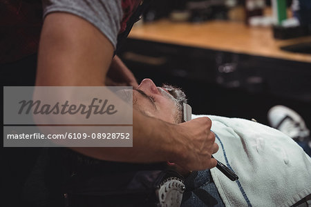 Man getting his beard shaved with razor in barber shop