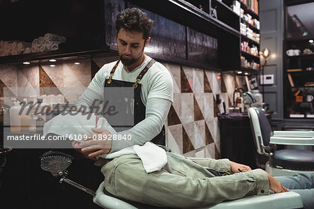 Barber applying a hot towel on a client face in barber shop