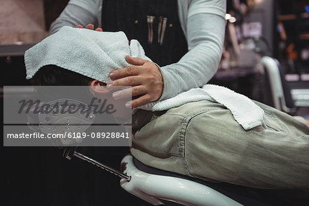 Mid section on barber wiping clients face with hot towel in barber shop