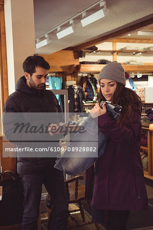 Woman selecting apparel in a clothes shop while man using mobile phone