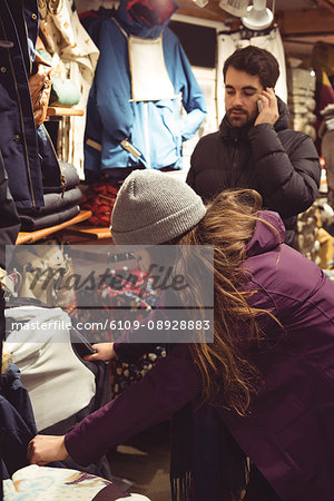 Woman selecting apparel in a clothes shop while man using mobile phone