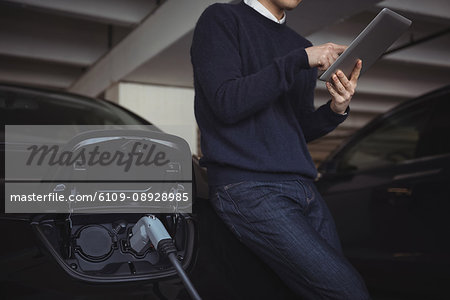 Man using digital tablet while charging electric car in garage
