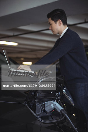 Man using laptop while charging electric car in garage