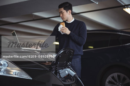 Man using laptop while charging electric car in garage