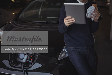 Man using digital tablet while charging electric car in garage