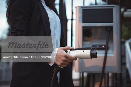 Mid section of woman holding car charger at electric vehicle charging station