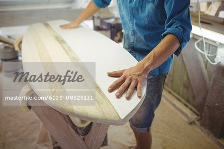Mid-section of man making surfboard in workshop