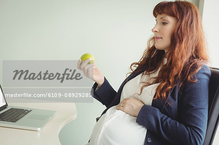 Pregnant businesswoman holding an apple in office