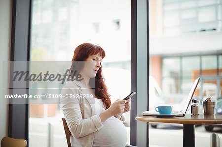 Pregnant businesswoman using mobile phone in office cafeteria