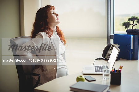 Pregnant businesswoman holding her back while sitting on chair in office