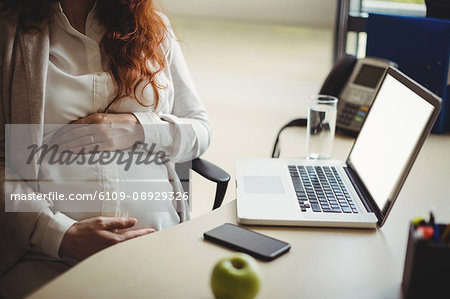 Mid-section of pregnant businesswoman holding her belly in office