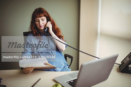 Pregnant businesswoman talking on telephone while working in office