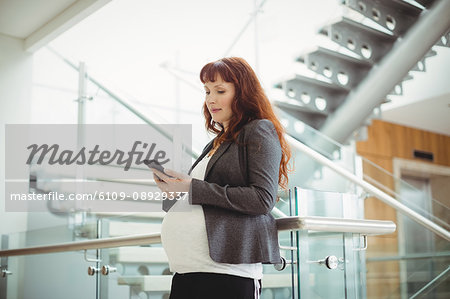 Pregnant businesswoman using mobile phone near staircase in office