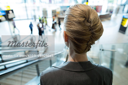 Rear view of businesswoman moving down on escalator at airport terminal