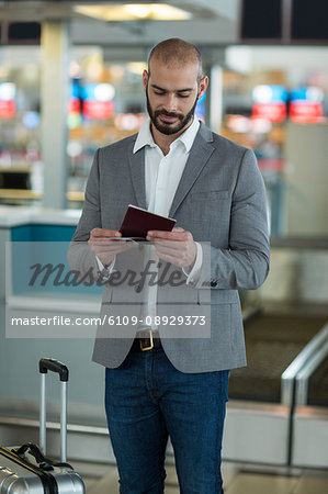 Businessman with luggage checking his boarding pass at airport terminal