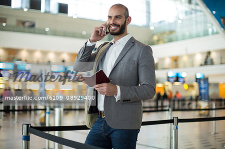 Smiling businessman holding a boarding pass and talking on mobile phone at airport terminal