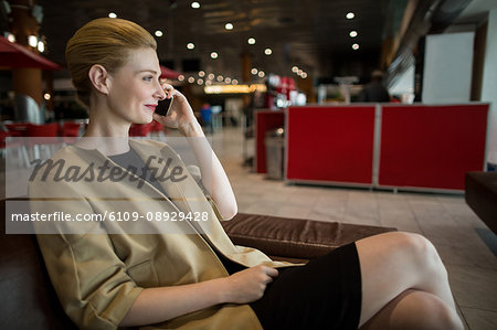 Businesswoman talking on mobile phone in waiting area at airport terminal