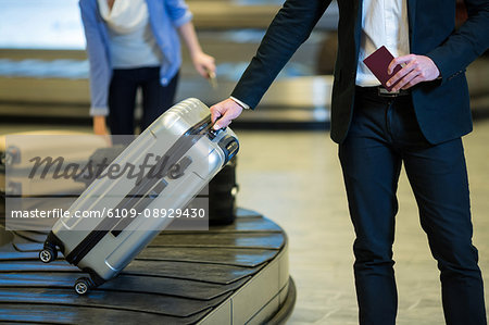 Mid section of businessman picking his luggage from baggage claim area at airport terminal