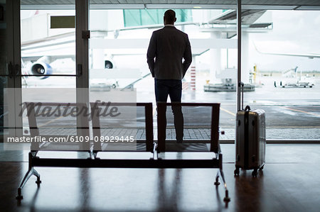 Rear view of businessman with luggage looking through glass window at airport