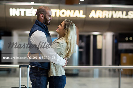 Cheerful couple embracing each other in waiting area at airport terminal