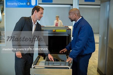 Airport security officer interacting with commuter while checking a package in airport terminal