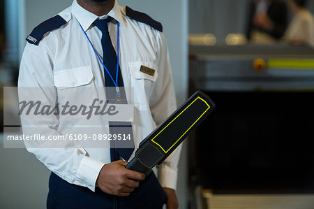 Mid section of airport security officer holding metal detector in airport terminal