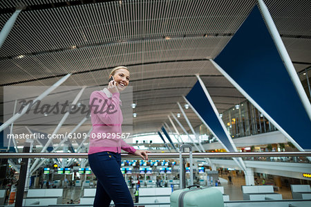 Female commuter with luggage talking on mobile phone in airport