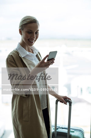 Businesswoman with luggage using mobile phone at airport