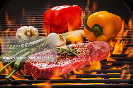 Beef steak with rosemary, red and yellow peppers, fresh garlic and spring onions on a flaming barbecue