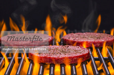 Raw hamburgers seasoned with salt and pepper on a flaming barbecue