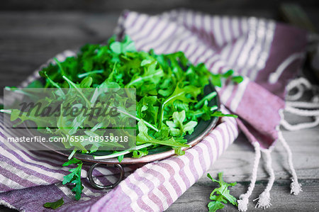 A bowl of rocket on a striped cloth A bowl of rocket on a striped cloth
