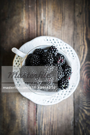 Fresh blackberries in a teacup on a wooden table