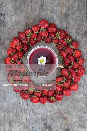 A cup of strawberry tea surrounded by fresh strawberries (seen from above)