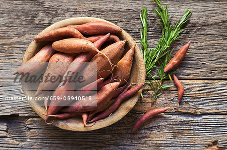 Sweet potatoes in a wooden bowl with sprigs of rosemary Sweet potatoes in a wooden bowl with sprigs of rosemary