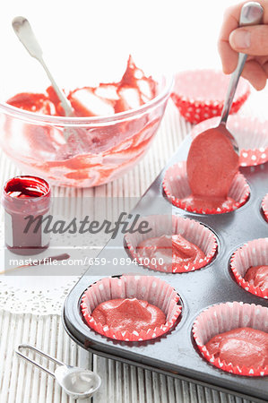 Red velvet cake batter being filled into paper cupcake cases