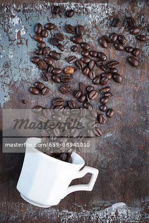 Coffee beans scattered over a rustic surface with a white coffee cup
