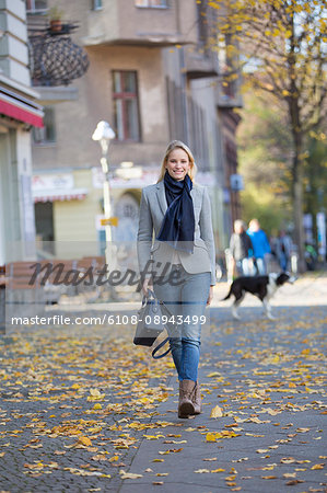 Pretty elegant woman walking with handbag in citycenter and smiling at camera