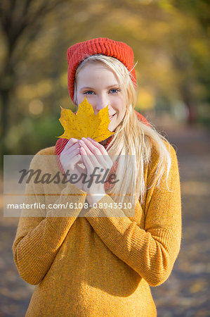 Portrait of a pretty blonde woman in park in autumn with leaf covering partially her face