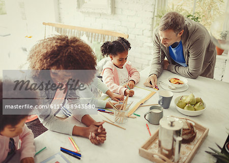 Multi-ethnic young family coloring with markers at table