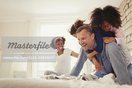 Multi-ethnic daughters tackling father on bed