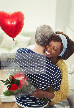 Wife receiving Valentine's Day rose bouquet and balloon, hugging husband