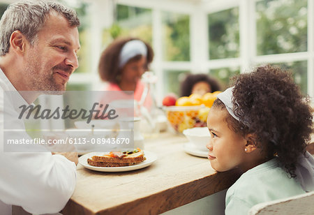 Multi-ethnic father and daughter playing staring game at kitchen table