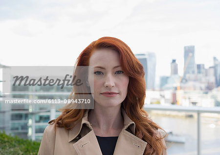 Portrait serious, confident businesswoman with red hair on urban balcony with city view