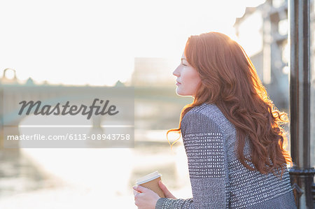 Serene businesswoman with red hair drinking coffee at urban waterfront