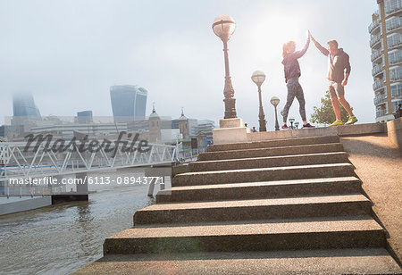 Runners high-fiving on sunny urban steps