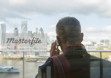 Businessman talking on cell phone on urban balcony with city view, London, UK